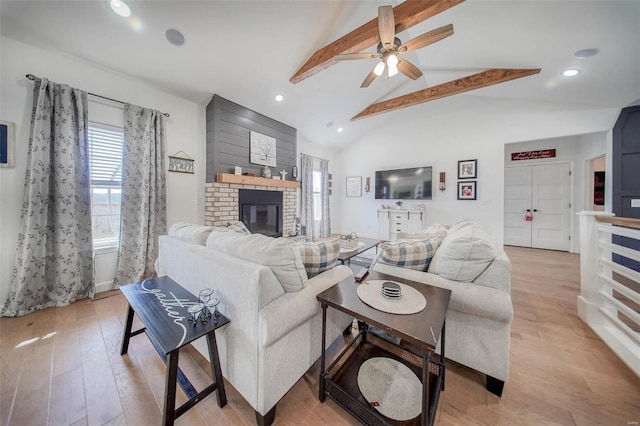 living room featuring ceiling fan, a brick fireplace, lofted ceiling with beams, and light hardwood / wood-style flooring