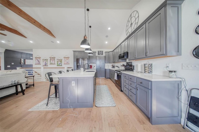 kitchen featuring stainless steel appliances, a kitchen breakfast bar, an island with sink, decorative light fixtures, and light wood-type flooring