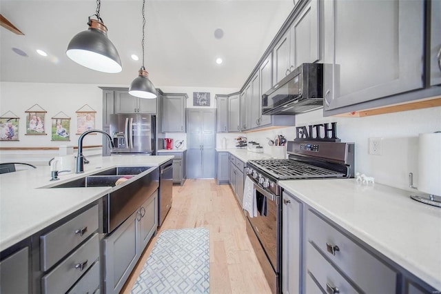 kitchen featuring sink, gray cabinetry, hanging light fixtures, light wood-type flooring, and appliances with stainless steel finishes