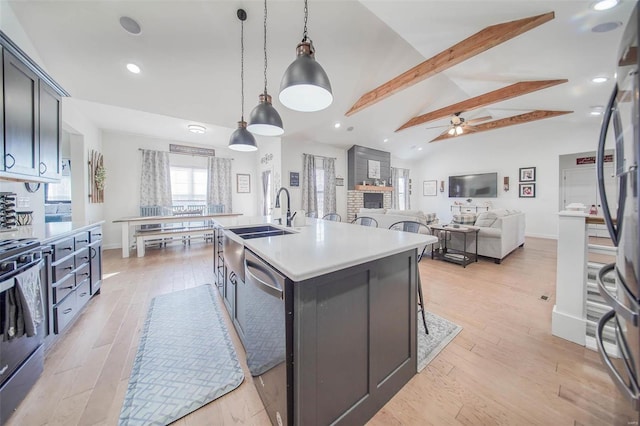 kitchen with lofted ceiling with beams, hanging light fixtures, a kitchen island with sink, stainless steel appliances, and light hardwood / wood-style flooring