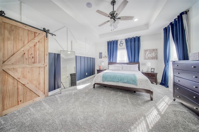 bedroom with ceiling fan, a tray ceiling, a barn door, and carpet