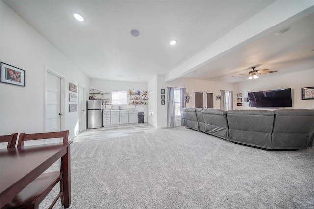 carpeted living room with ceiling fan, beam ceiling, and sink