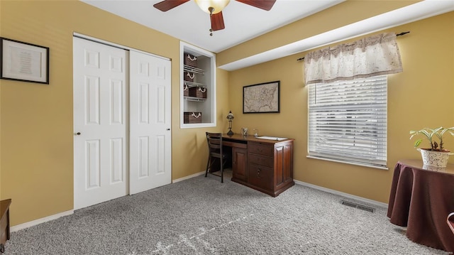 carpeted home office with built in shelves and ceiling fan