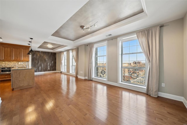 unfurnished living room featuring hardwood / wood-style flooring, a raised ceiling, and ornamental molding