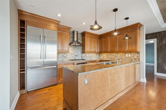 kitchen featuring sink, hanging light fixtures, stainless steel appliances, wall chimney range hood, and kitchen peninsula