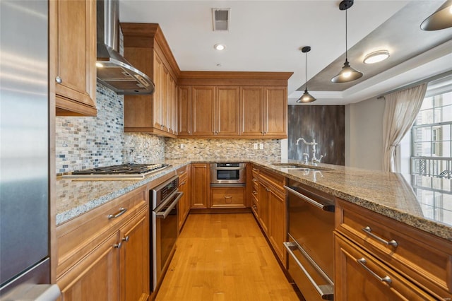 kitchen featuring sink, hanging light fixtures, light hardwood / wood-style flooring, wall chimney exhaust hood, and stainless steel appliances