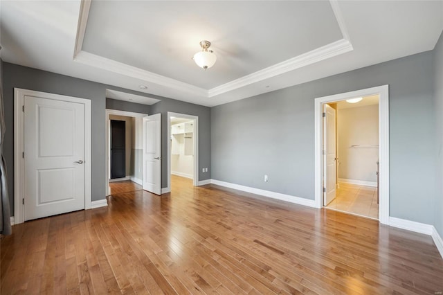 unfurnished bedroom with light wood-type flooring, a walk in closet, a raised ceiling, connected bathroom, and a closet