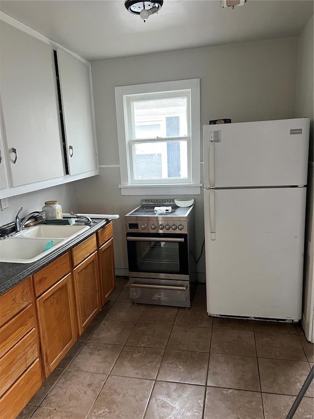 kitchen featuring tile patterned floors, sink, stainless steel stove, and white refrigerator