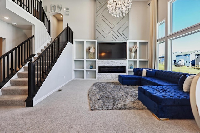 living room featuring stairway, carpet, a glass covered fireplace, and a towering ceiling