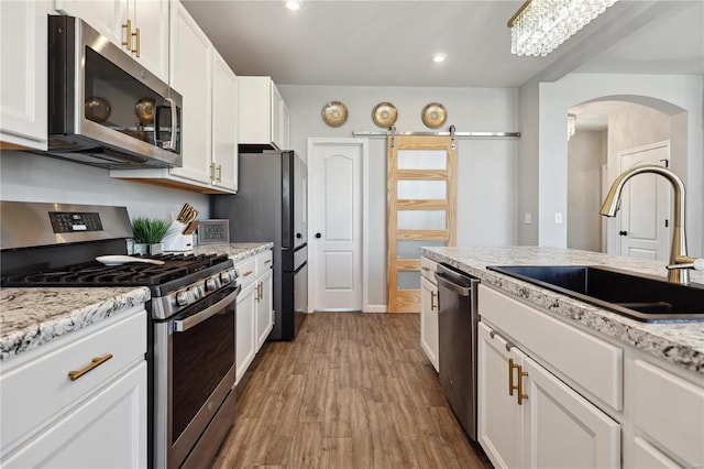 kitchen with a barn door, wood finished floors, a sink, white cabinetry, and appliances with stainless steel finishes