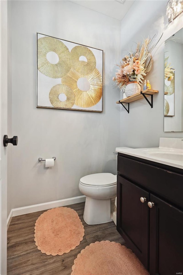 half bathroom featuring vanity, wood finished floors, toilet, and baseboards