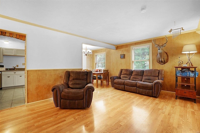 living room with an inviting chandelier, sink, wooden walls, ornamental molding, and light hardwood / wood-style floors