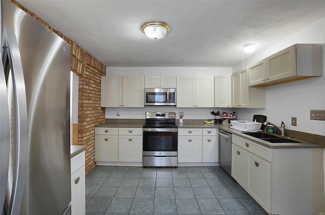 kitchen with a textured ceiling, stainless steel appliances, sink, white cabinets, and light tile patterned flooring