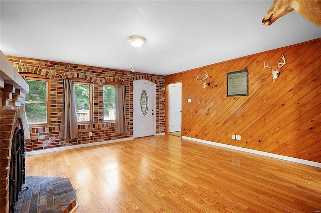 unfurnished living room featuring wood walls, light hardwood / wood-style floors, a fireplace, and brick wall