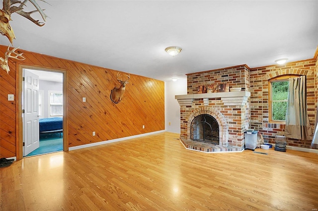 unfurnished living room featuring wooden walls, a fireplace, a healthy amount of sunlight, and wood-type flooring