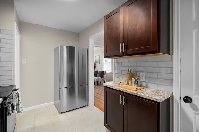 kitchen with tasteful backsplash, light stone counters, dark brown cabinets, and appliances with stainless steel finishes