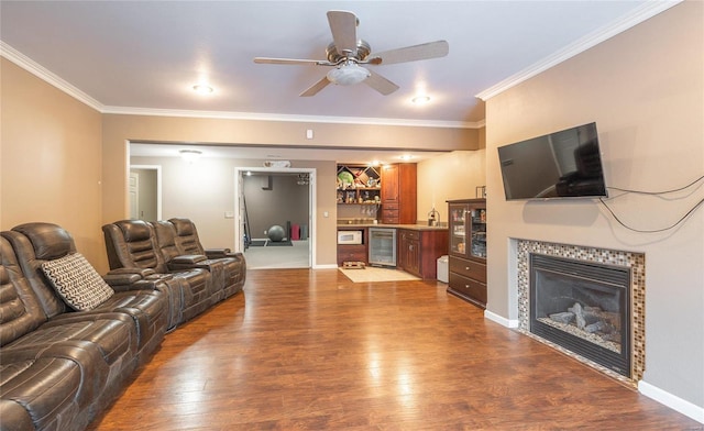 living room featuring a tiled fireplace, wood-type flooring, ornamental molding, and wine cooler