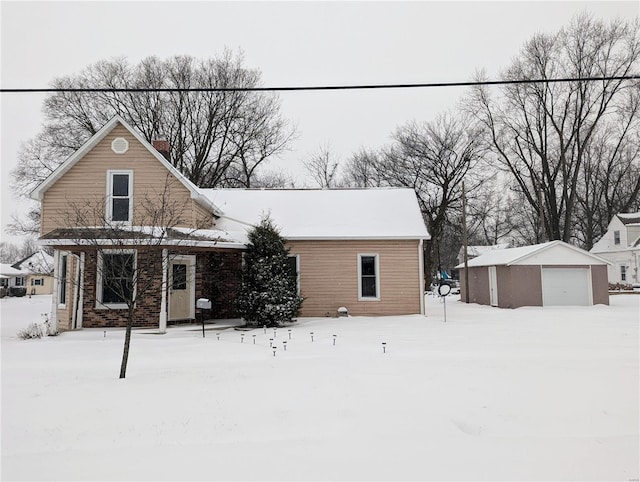 snow covered back of property with an outdoor structure and a garage