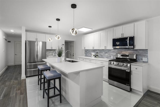 kitchen featuring white cabinets, sink, an island with sink, appliances with stainless steel finishes, and decorative light fixtures