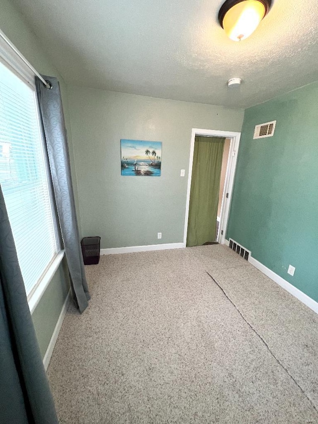 unfurnished room with a textured ceiling, carpet, and visible vents