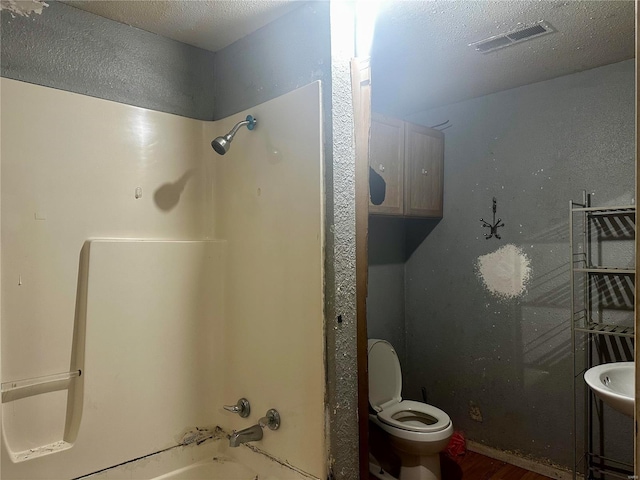 bathroom featuring shower / bathing tub combination, toilet, hardwood / wood-style floors, and a textured ceiling