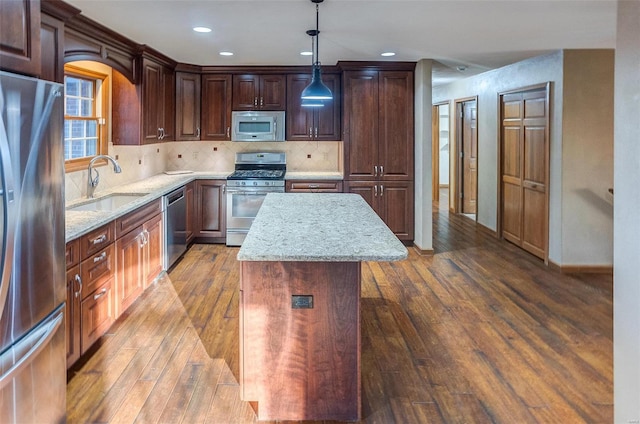 kitchen featuring dark wood-type flooring, sink, hanging light fixtures, appliances with stainless steel finishes, and a kitchen island