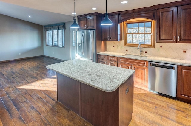 kitchen featuring sink, decorative light fixtures, light wood-type flooring, appliances with stainless steel finishes, and a kitchen island