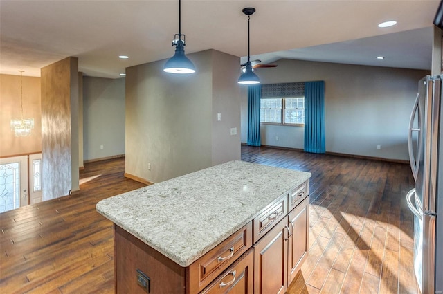 kitchen with lofted ceiling, decorative light fixtures, stainless steel fridge, a kitchen island, and light stone countertops