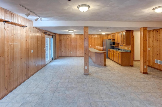 kitchen with stainless steel refrigerator, rail lighting, sink, and wood walls