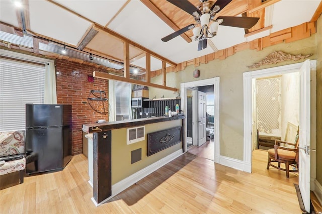 kitchen with black refrigerator, light hardwood / wood-style floors, ceiling fan, and brick wall