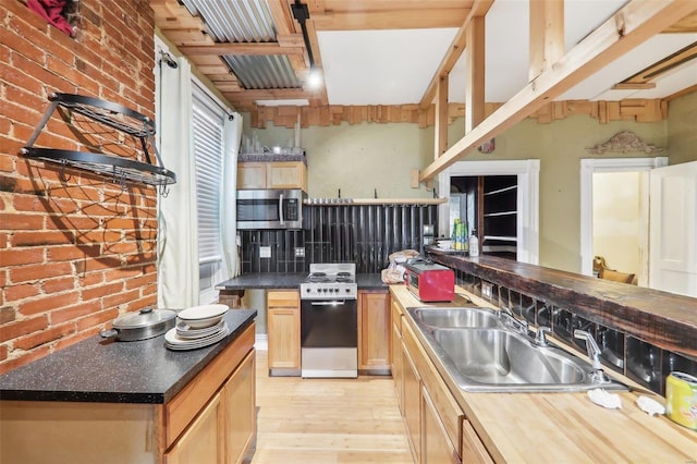 kitchen featuring stove, light hardwood / wood-style floors, brick wall, and sink