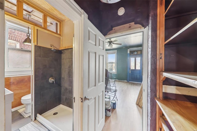 bathroom with a tile shower, hardwood / wood-style flooring, ceiling fan, and toilet