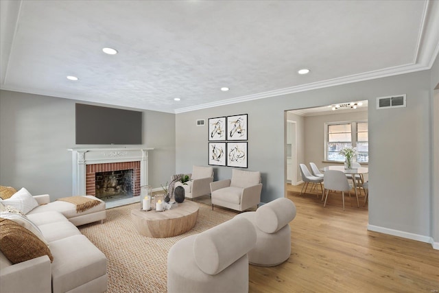 living room with a brick fireplace, ornamental molding, and light hardwood / wood-style flooring