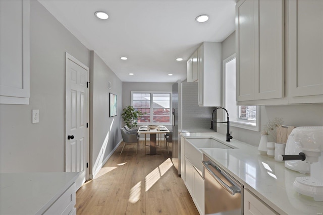 kitchen featuring white cabinetry, appliances with stainless steel finishes, light stone countertops, light hardwood / wood-style flooring, and sink