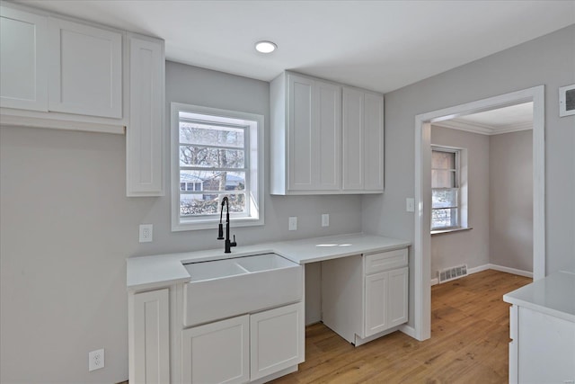 kitchen featuring ornamental molding, light hardwood / wood-style flooring, white cabinets, and sink