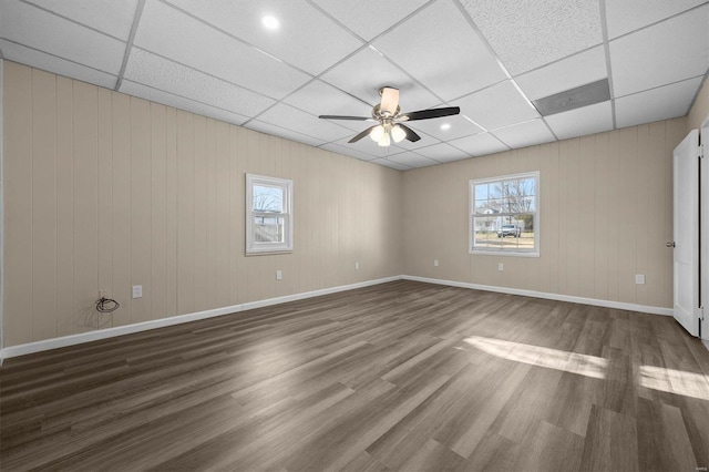 empty room with a paneled ceiling, ceiling fan, dark hardwood / wood-style floors, and plenty of natural light