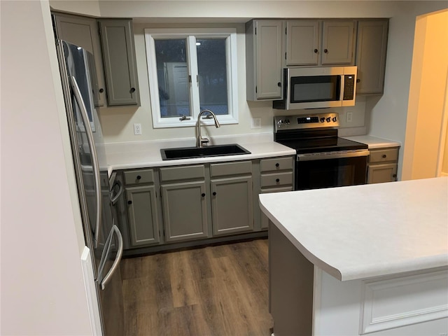 kitchen featuring kitchen peninsula, appliances with stainless steel finishes, dark wood-type flooring, sink, and gray cabinets