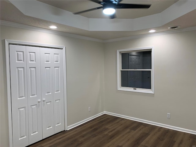 unfurnished bedroom with ceiling fan, dark hardwood / wood-style floors, ornamental molding, a tray ceiling, and a closet