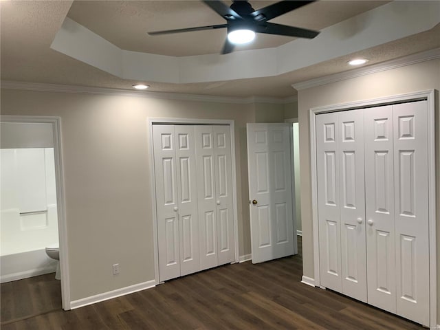 unfurnished bedroom with ceiling fan, ensuite bath, a tray ceiling, and multiple closets