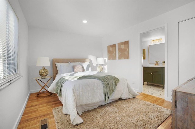 bedroom with light hardwood / wood-style floors, ensuite bath, and sink