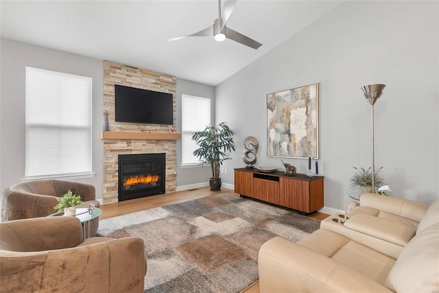 living area featuring a stone fireplace, vaulted ceiling, wood finished floors, and baseboards