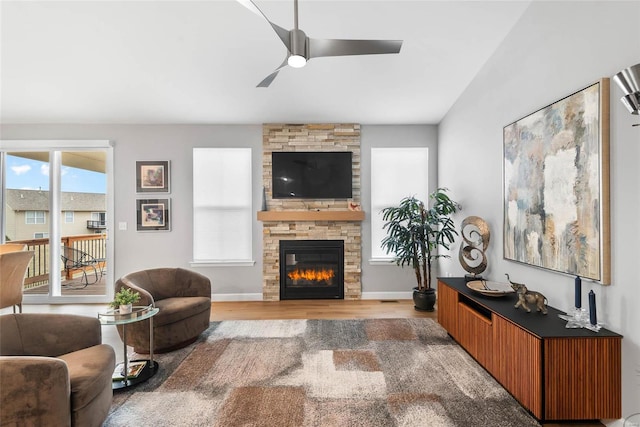 living area with a stone fireplace, wood finished floors, baseboards, and a ceiling fan