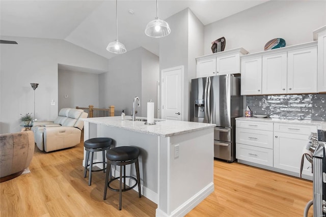 kitchen featuring a sink, stainless steel appliances, white cabinets, a kitchen bar, and open floor plan