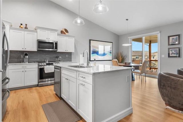 kitchen with light wood finished floors, light stone counters, stainless steel appliances, white cabinetry, and a sink