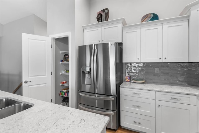 kitchen with light stone counters, decorative backsplash, white cabinets, and stainless steel fridge with ice dispenser