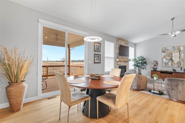 dining area with visible vents, a ceiling fan, a stone fireplace, light wood finished floors, and baseboards