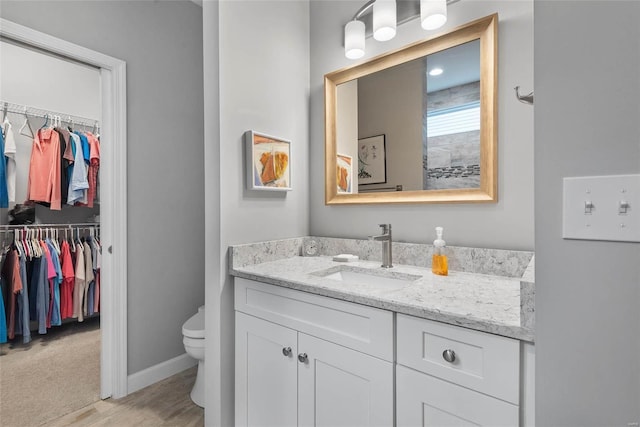 bathroom with vanity, a spacious closet, toilet, and baseboards