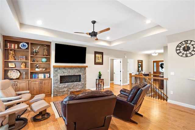 living room featuring built in shelves, a tray ceiling, ceiling fan, a fireplace, and light hardwood / wood-style floors