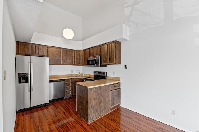 kitchen with a high ceiling, appliances with stainless steel finishes, sink, dark hardwood / wood-style floors, and kitchen peninsula