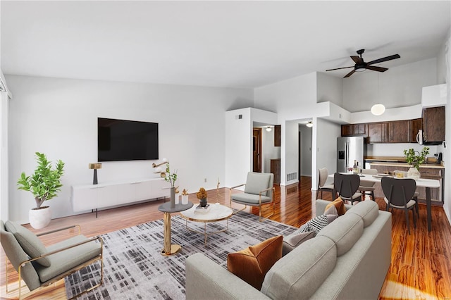 living room featuring ceiling fan, light hardwood / wood-style flooring, and a towering ceiling